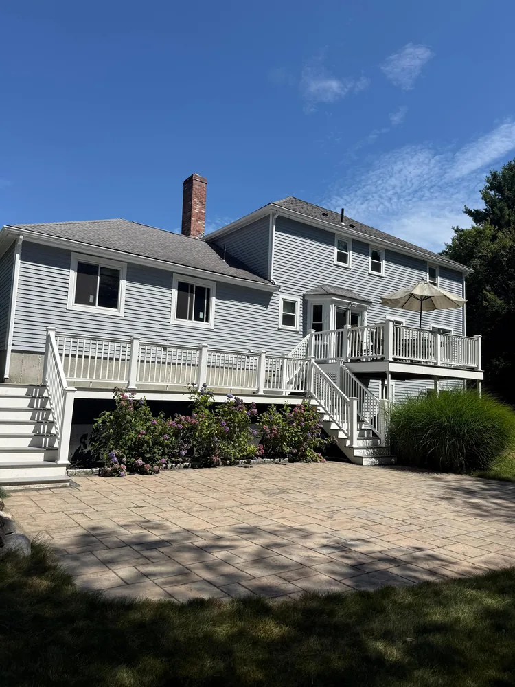 Back of a home with a white deck, a shaded seating area and a paver patio