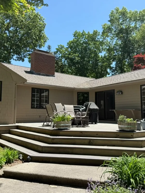 Backyard deck with wide steps and patio furniture behind a tan house