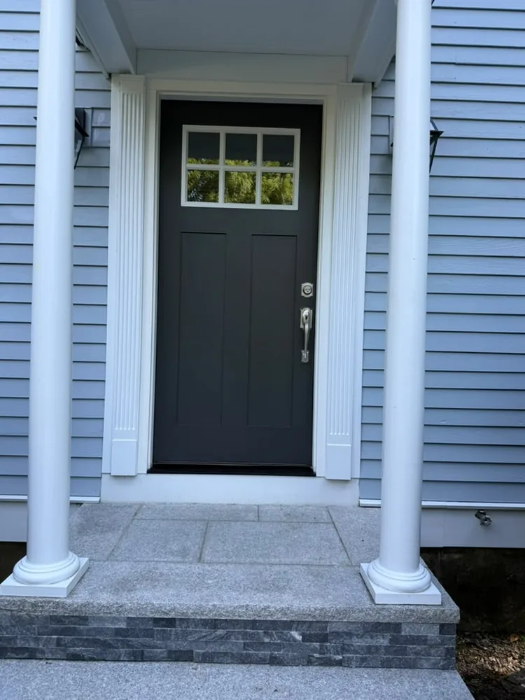 Black front door with a glass panel between white columns on a stone step