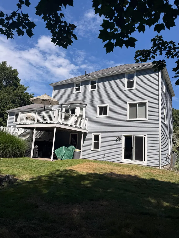 Rear elevation of a gray sided home with a raised deck and sliding doors