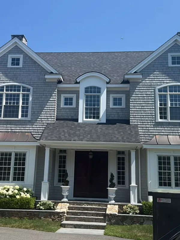 Front of a gray shingle home with white trim and arched dormers