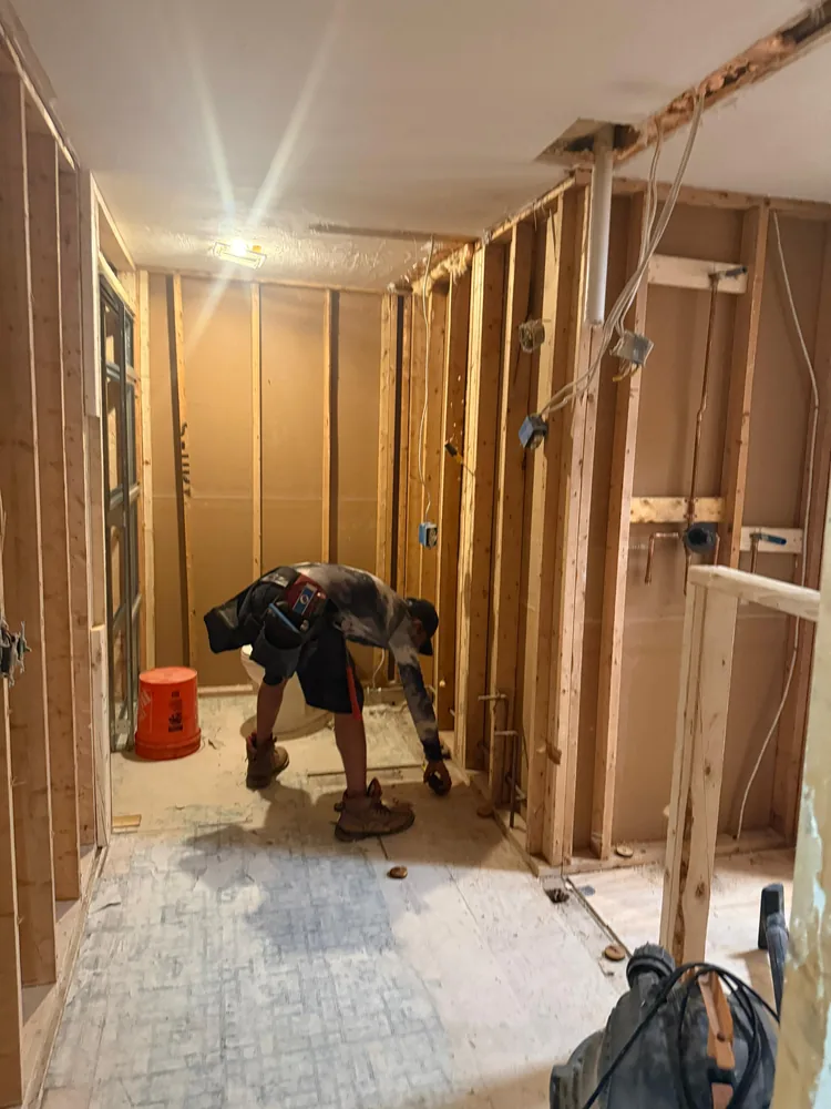 Interior stripped back to the studs during a full remodel, with a crew member at work