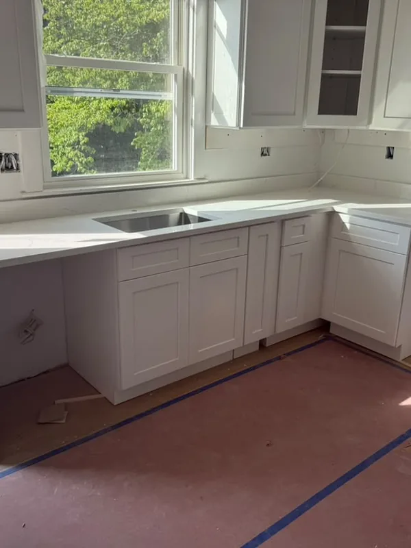 White cabinets being installed under a window, with the floor protected