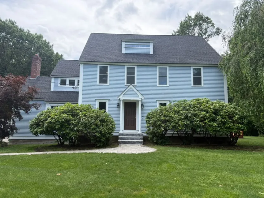 Light blue colonial with fresh white trim behind rounded shrubs