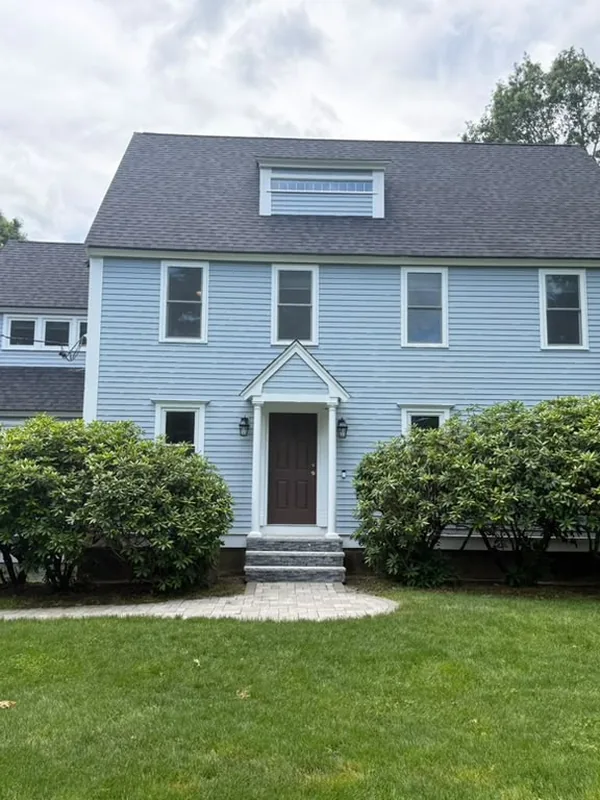 Light blue colonial with white trim behind rounded shrubs