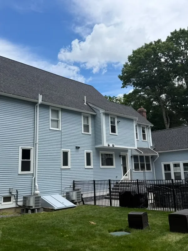 Rear of a light blue house with a black fence and a trimmed lawn