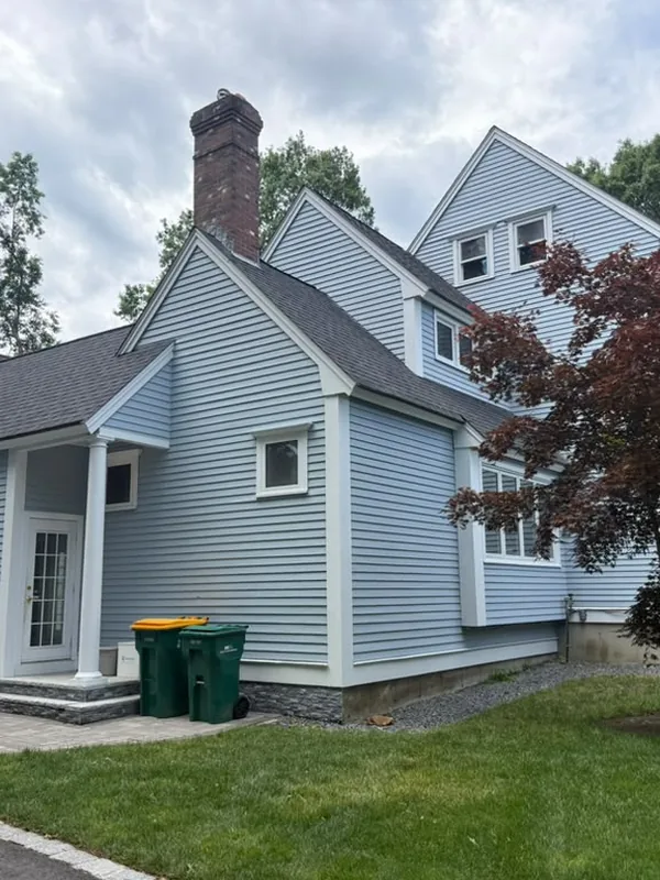 Side of a light blue house with a brick chimney and steep gables