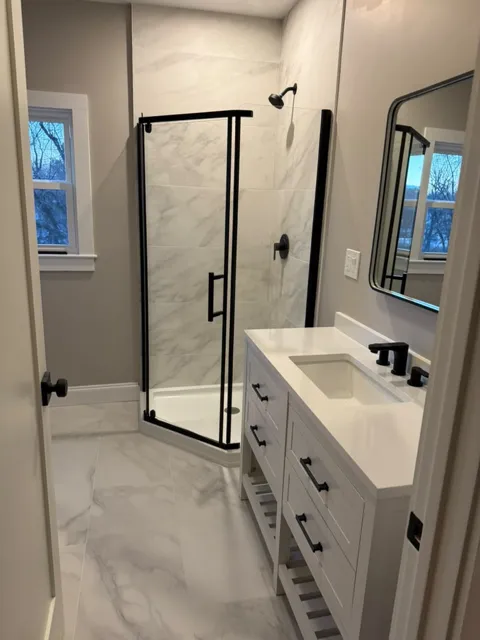 Remodeled bathroom with marble tile, a glass shower and black fixtures