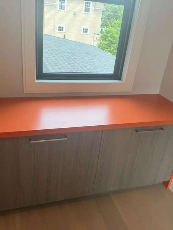 Built in cabinet with an orange top and side panels under a window
