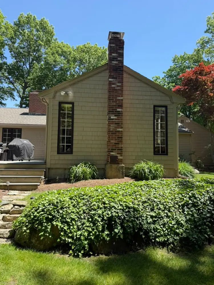 Tan house with a tall brick chimney and ivy along the foundation