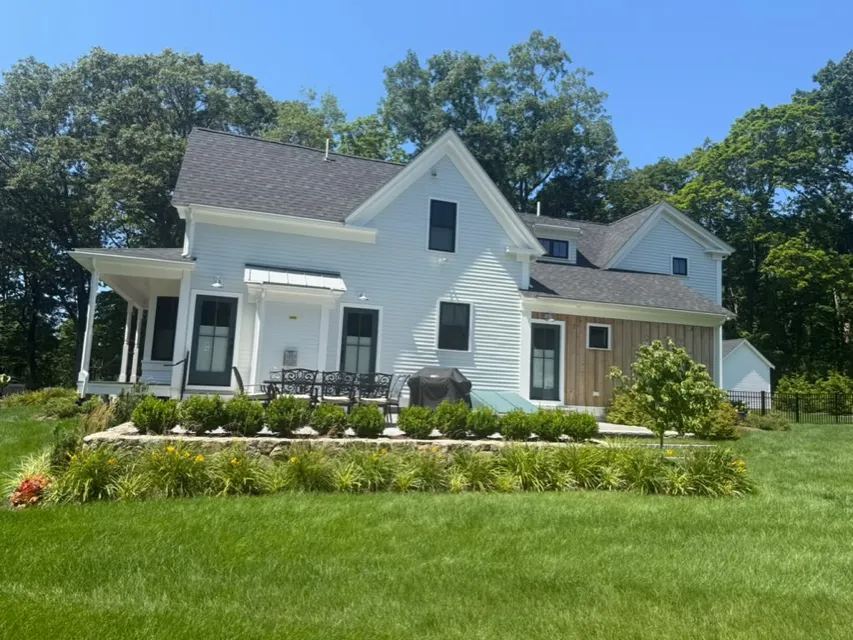 White farmhouse with a long front porch on a sunny day after exterior painting
