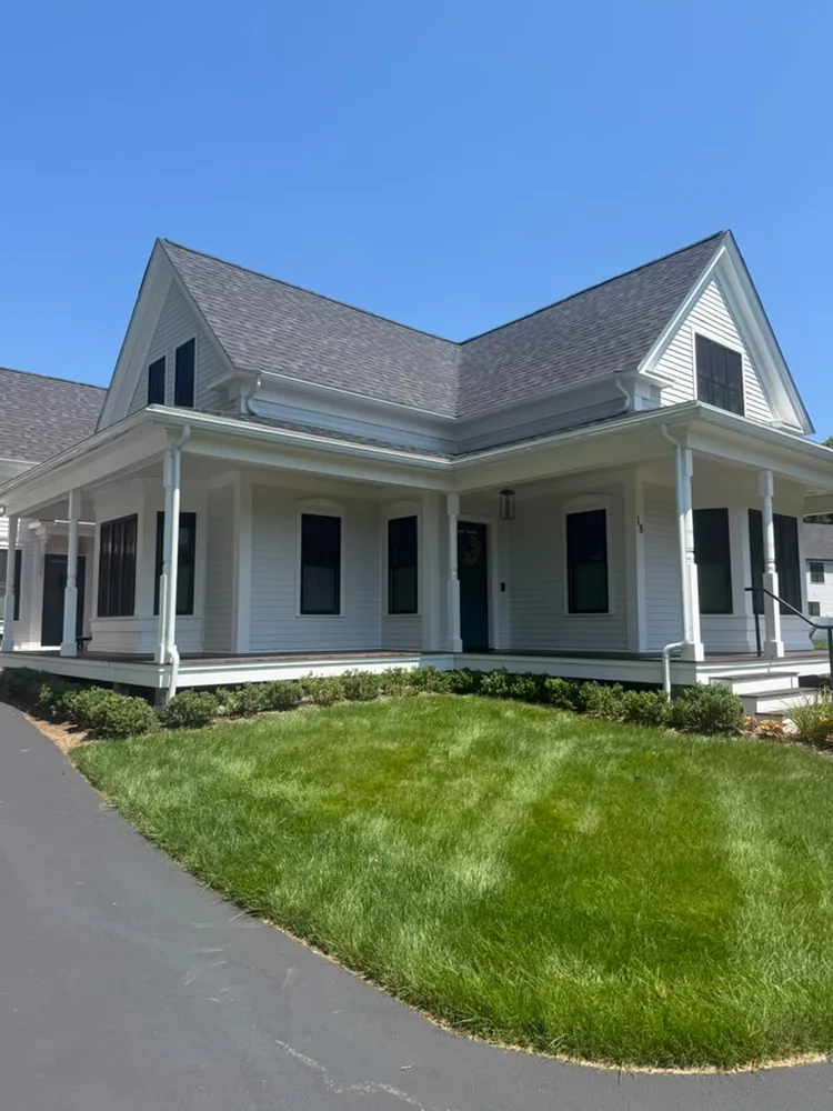 White house with a wraparound porch, black shutters and a fresh lawn