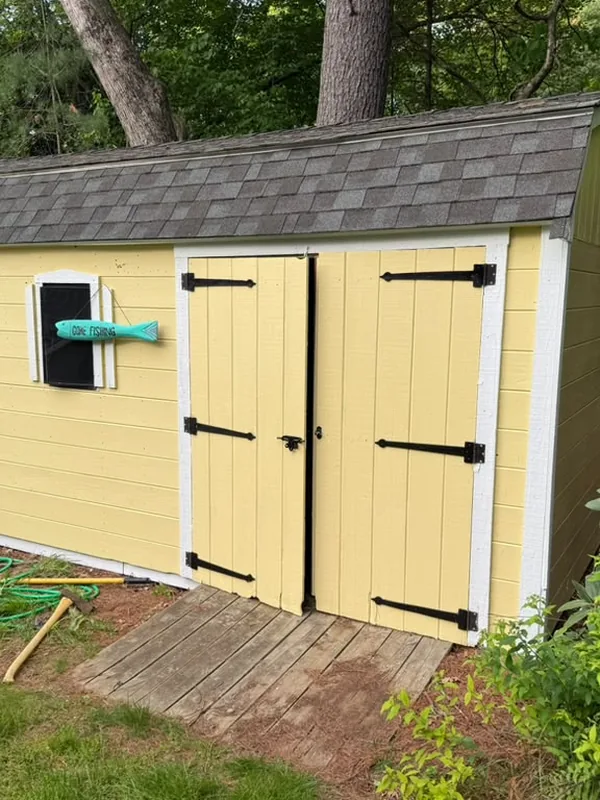 Yellow backyard shed with white trim and black hardware, seen from the side